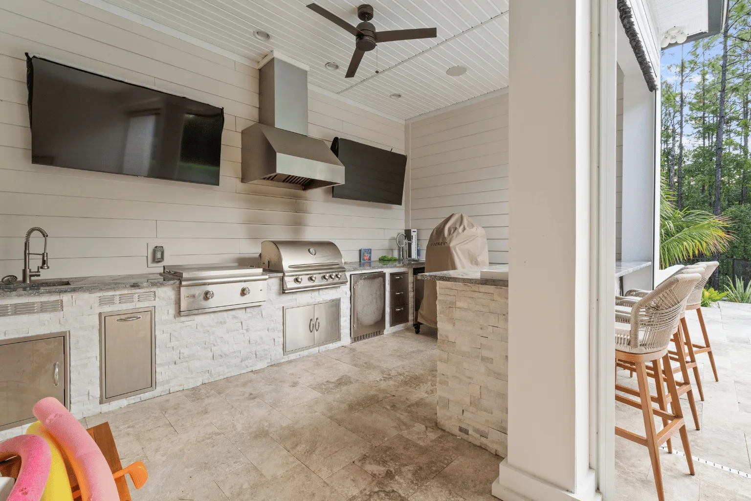 Custom outdoor kitchen installation with grill, range hood, TV, and bar seating by Jax Pavers in Jacksonville FL