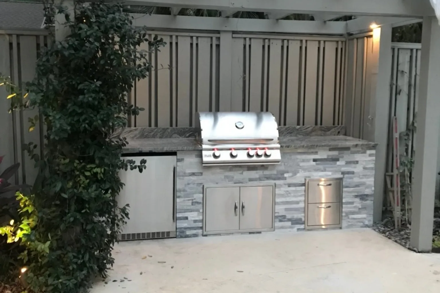 Outdoor kitchen with stacked stone veneer, built-in grill, and pergola lighting by Jax Pavers in Jacksonville FL