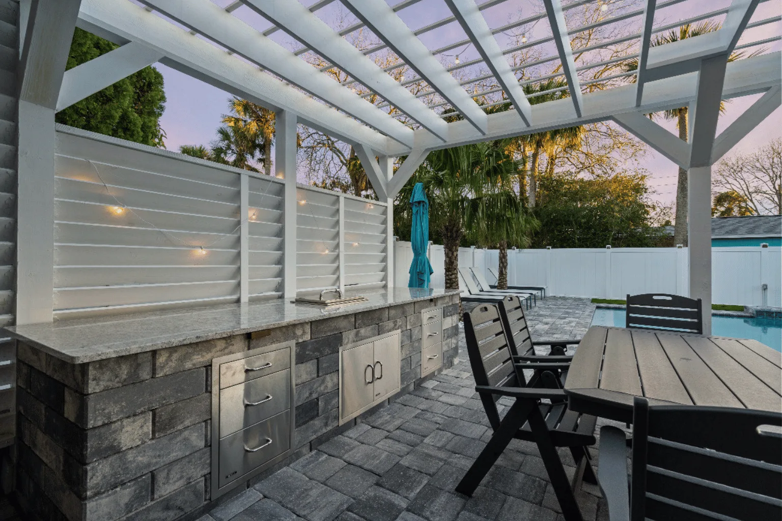 Outdoor kitchen and pergola installation with stone veneer base and poolside dining by Jax Pavers in Jacksonville FL